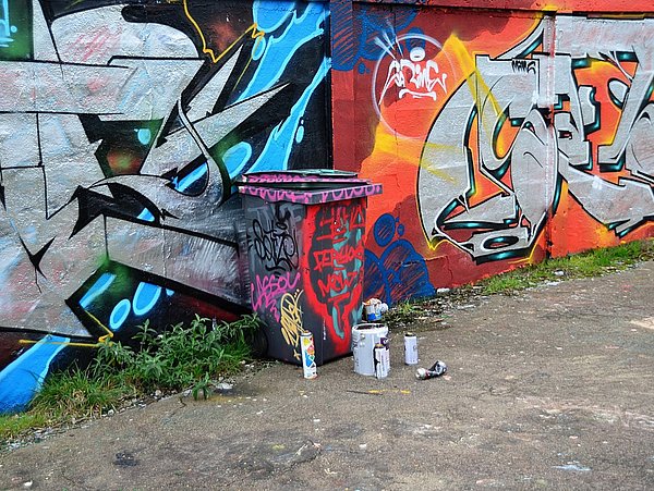 illegale Müllablagerung vor einer mit Graffiti besprühten Wand und Mülltonne